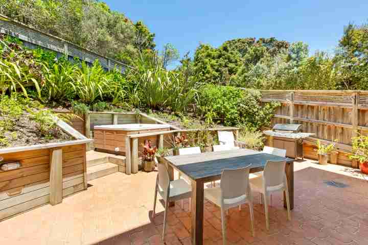Outdoor dining area in private courtyard with spa surrounded by New Zealand bush