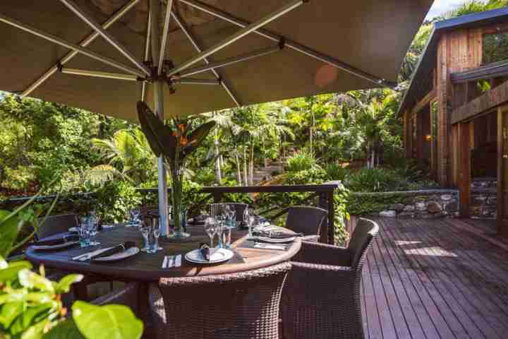 Sheltered outdoor dining on sunny deck at luxury Waiheke lodge, Kauri Springs